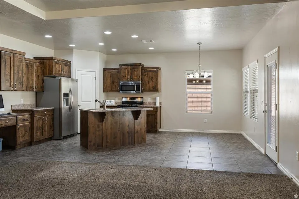 Kitchen featuring rich wood cabinetry, stainless steel appliances, a central island with sink, recessed lighting, and tile flooring