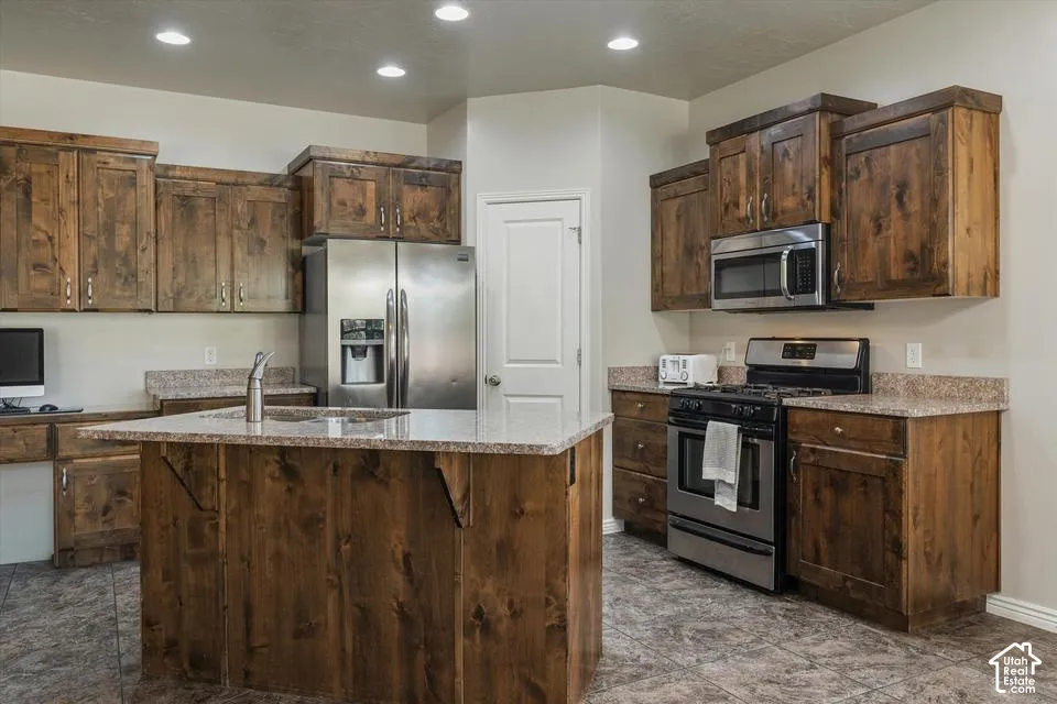 Kitchen featuring wood cabinetry, stainless steel appliances, a center island with sink, granite-style countertops, and recessed lighting