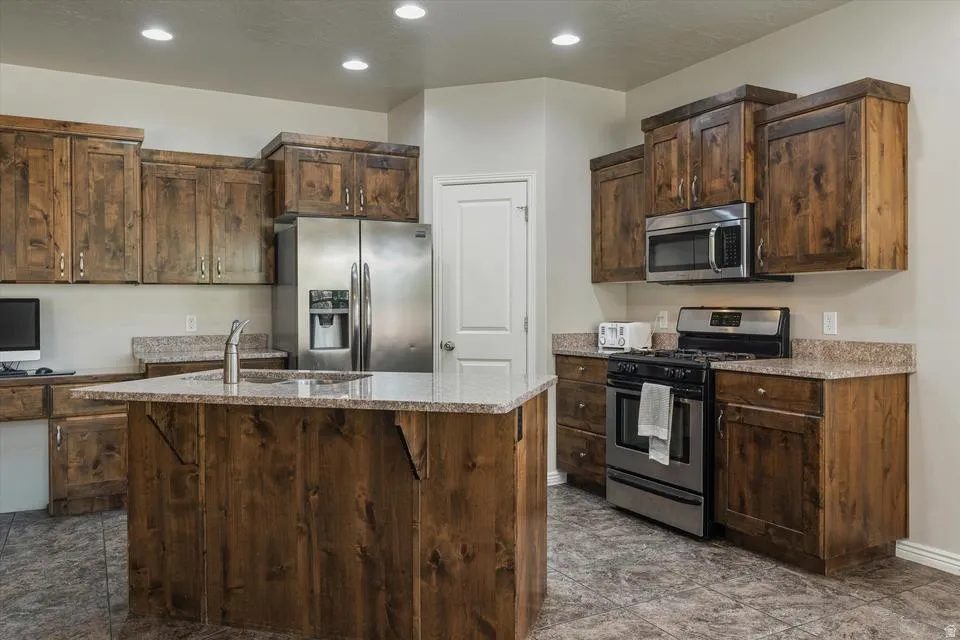 Kitchen featuring wood cabinetry, stainless steel appliances, a center island with sink, granite-style countertops, and recessed lighting