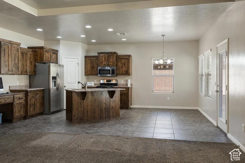 Kitchen featuring rich wood cabinetry, stainless steel appliances, a central island with sink, recessed lighting, and tile flooring