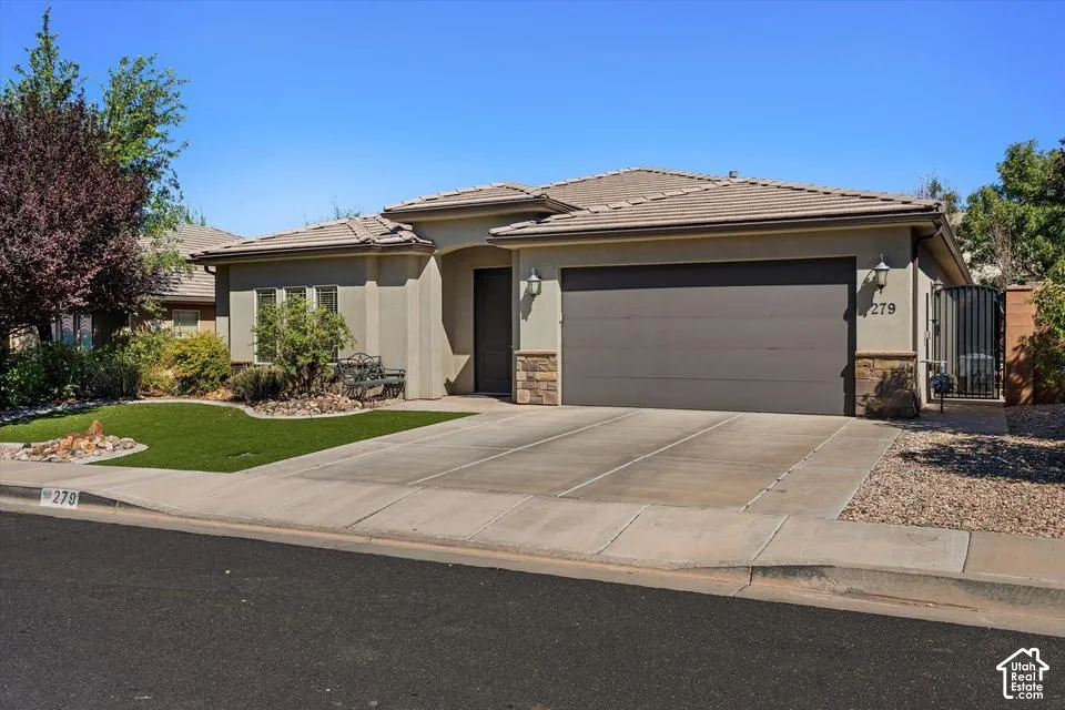 Stucco exterior with stone accents, tile roof, attached garage, and a gated side entrance