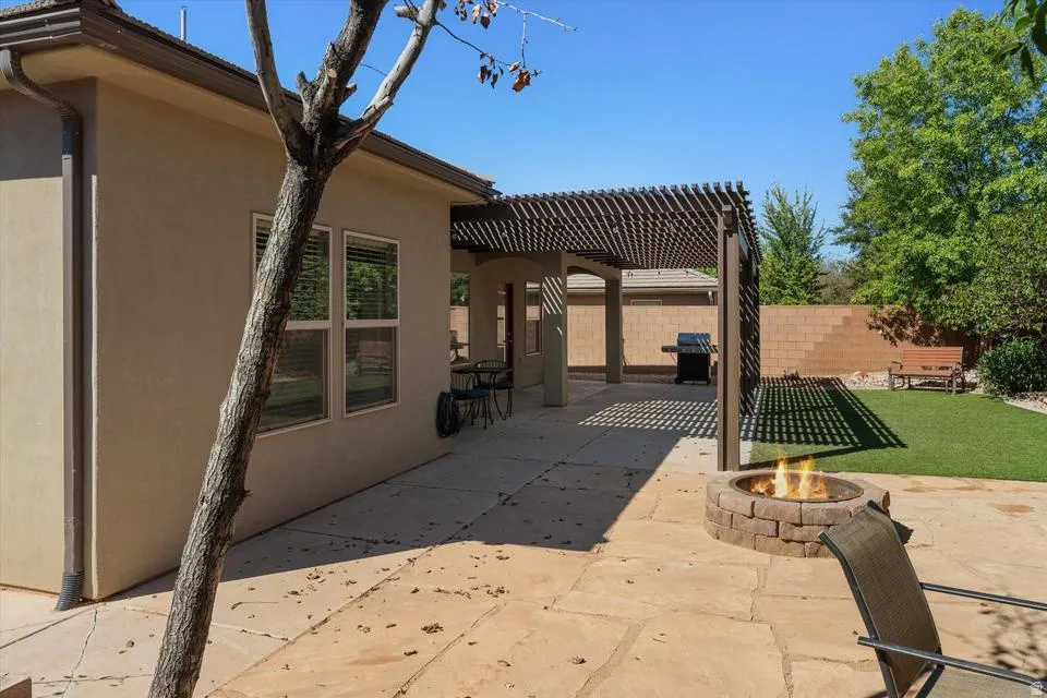 Expansive flagstone patio with a built-in fire pit, covered pergola, and a manicured lawn