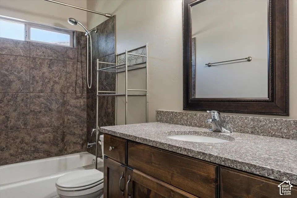 Brown tiled shower surround, white bathtub, wood-finish vanity, light-colored speckled countertop, and framed mirror