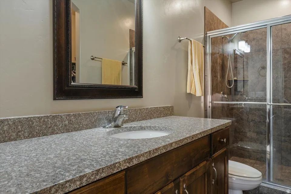 Bathroom featuring a wood-finish vanity with an integrated sink, a speckled countertop, a framed wall mirror, and a glass-enclosed shower with tiled walls