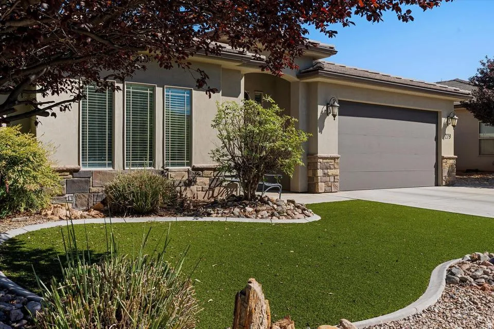Stucco exterior with stone accents, covered entry, attached garage with decorative sconces, and artificial turf landscaping with rock beds