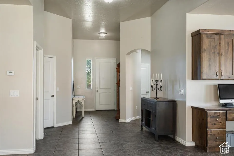 Entryway featuring tile flooring, a built-in wood-finish desk, wood-finish cabinetry, and an arched doorway