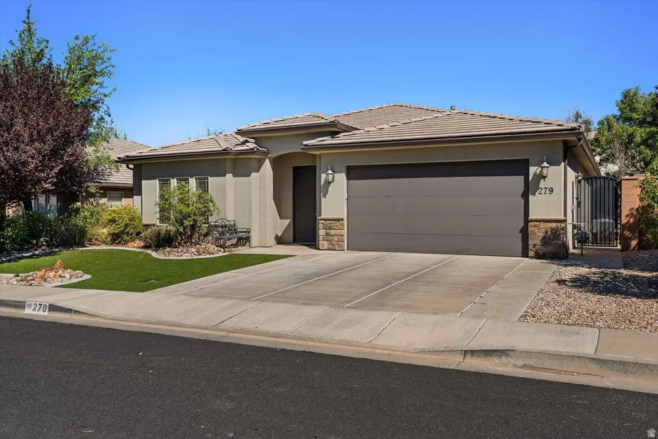Stucco exterior with stone accents, tile roof, attached garage, and a gated side entrance