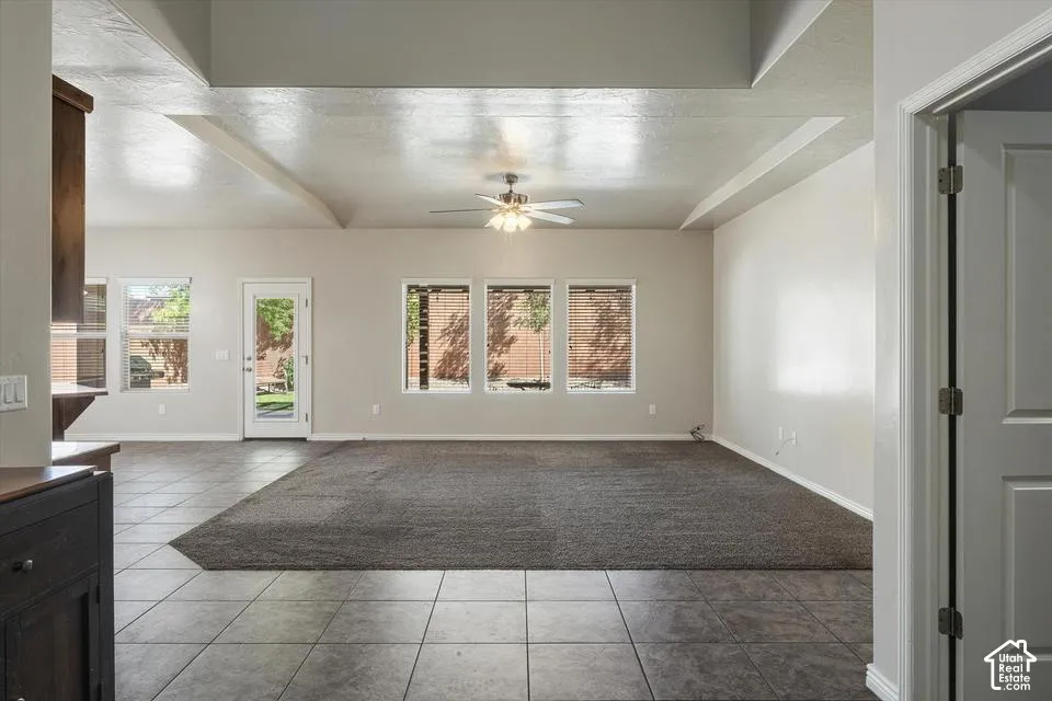 Tray ceiling with exposed beams, ceiling fan, multiple windows with blinds, tiled flooring, and carpeted area