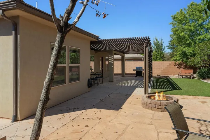 Expansive flagstone patio with a built-in fire pit, covered pergola, and a manicured lawn