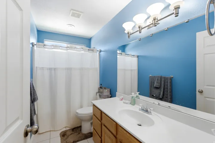 Bathroom featuring a vanity with a white countertop and integrated sink, wood-finish cabinetry, and a full-width mirror with a three-light fixture above