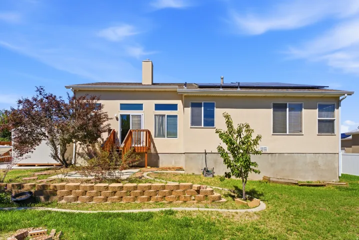 Exterior featuring a stucco finish, a rear deck with wood railing, a patio door, multiple windows, and solar panels on the roof