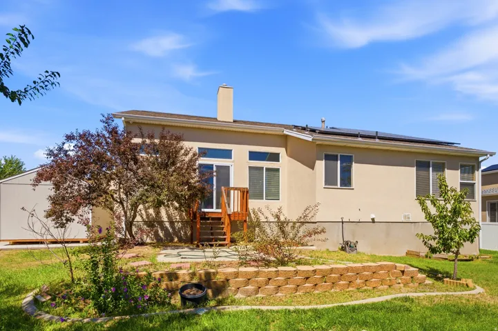 Stucco exterior with multiple windows, rooftop solar panels, wood deck, and a retaining wall