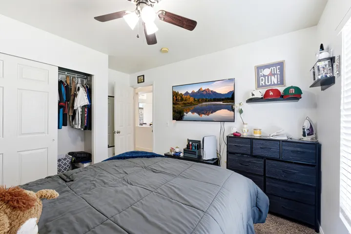 White walls, ceiling fan with light fixture, carpeted flooring, and a closet with bi-fold doors