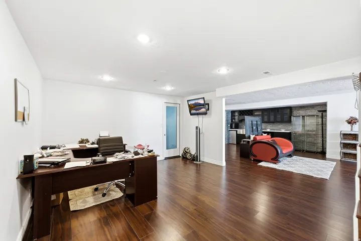 Recessed lighting, wood-finish flooring, white walls, and an open concept layout with a wet bar featuring dark cabinetry and a tile backsplash