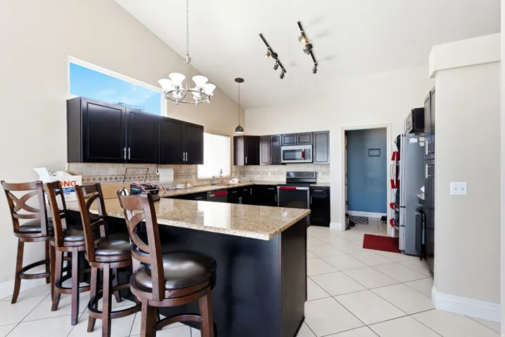 Kitchen featuring vaulted ceilings, an eat-at island with a stone-finish countertop, black cabinetry, white tile flooring, and a large transom window