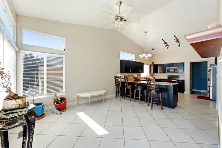 Vaulted ceilings with a ceiling fan, tile flooring, kitchen with dark cabinetry and peninsula seating, and large windows with upper transom windows