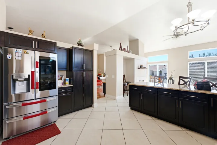 Kitchen featuring dark wood-finish cabinetry, stainless steel refrigerator, light-toned tile flooring, and a stone-finish countertop island