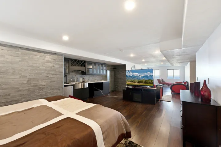 Stone accent wall with built-in wet bar, wood-finish flooring, recessed lighting, and multiple windows
