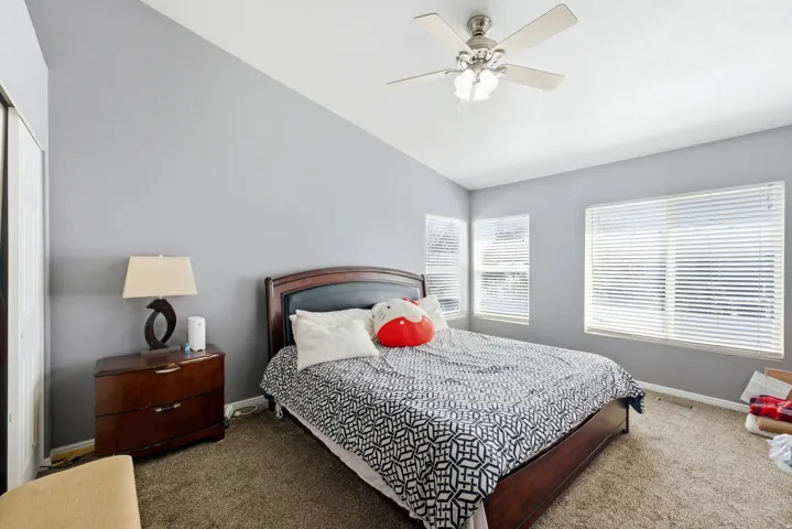 Vaulted ceiling, ceiling fan with integrated lighting, multiple windows with blinds, built-in closet with bifold doors, and carpet flooring