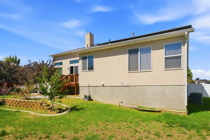Stucco exterior with a wood deck, sliding glass doors, multiple windows, and a landscaped retaining wall