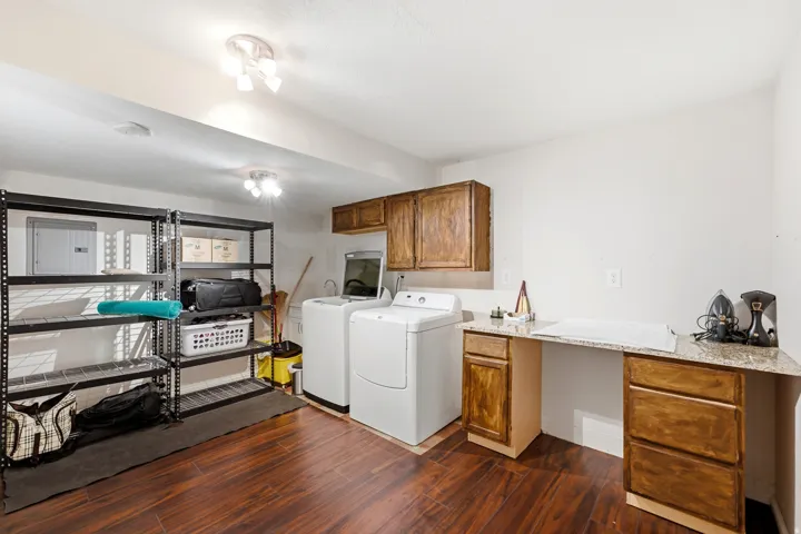 Laundry area featuring wood-finish flooring, overhead lighting, and built-in cabinetry with a countertop