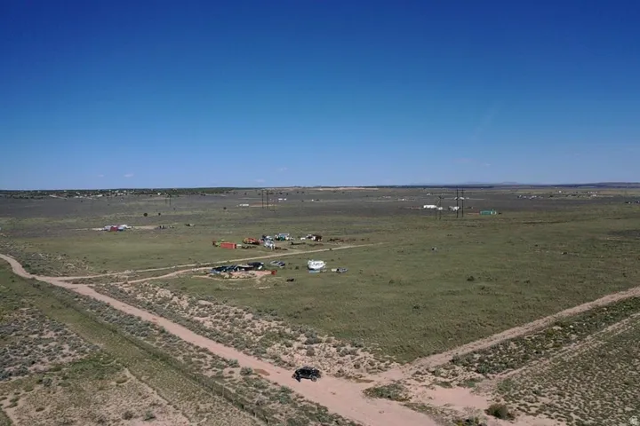 Expansive open land featuring a dirt road, minimal vegetation, and distant structures under a clear sky