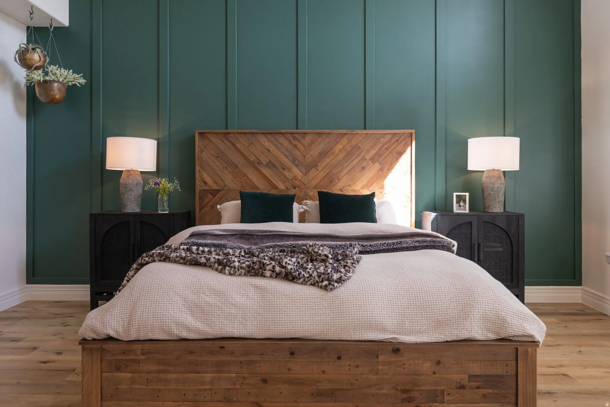 Wood-finish flooring with white baseboards, a wood-paneled accent wall, and a wooden bed frame with a chevron-patterned headboard