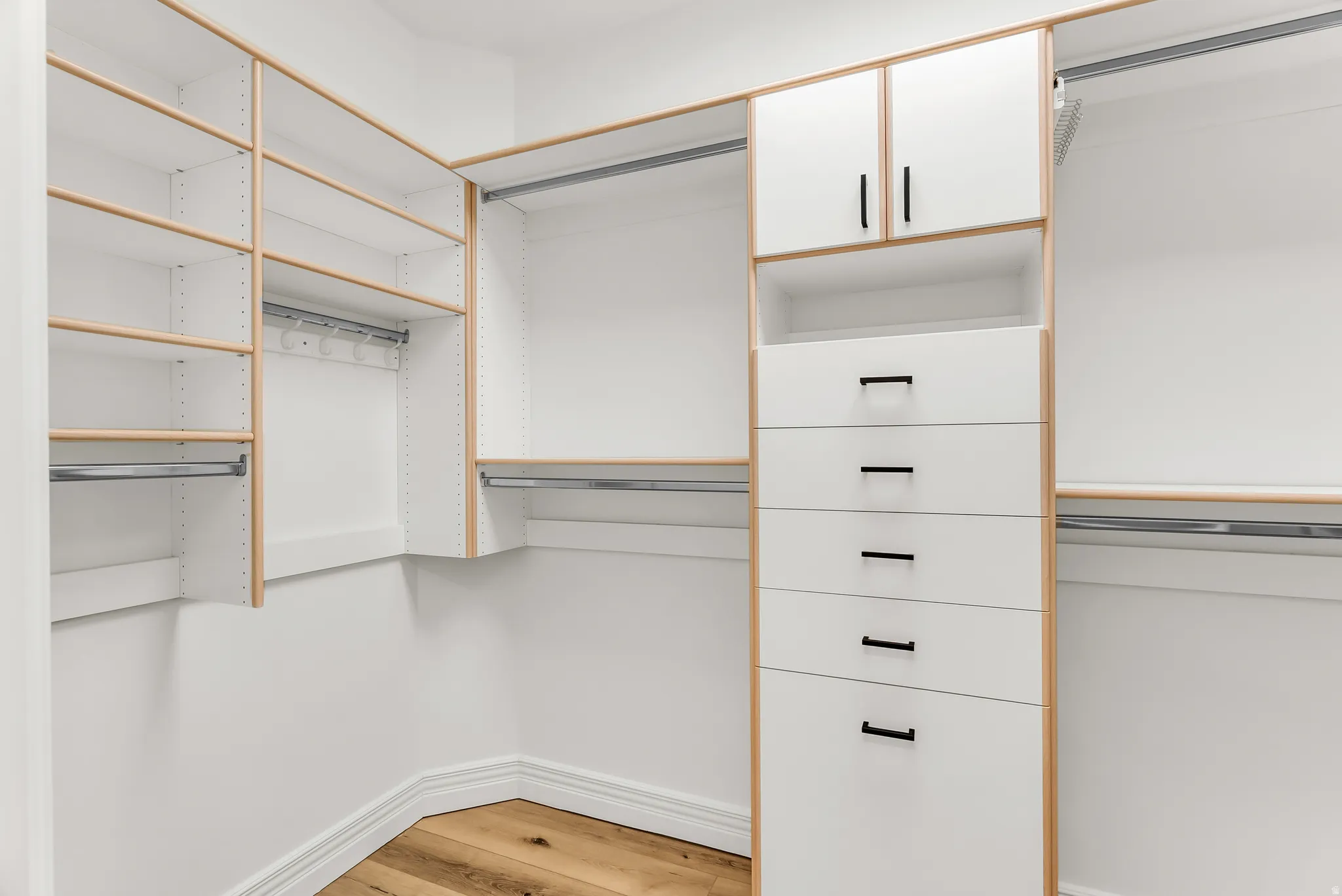 Custom closet system featuring wood-finish accents, white cabinetry, extensive shelving, hanging rods, and integrated drawers with matte black hardware