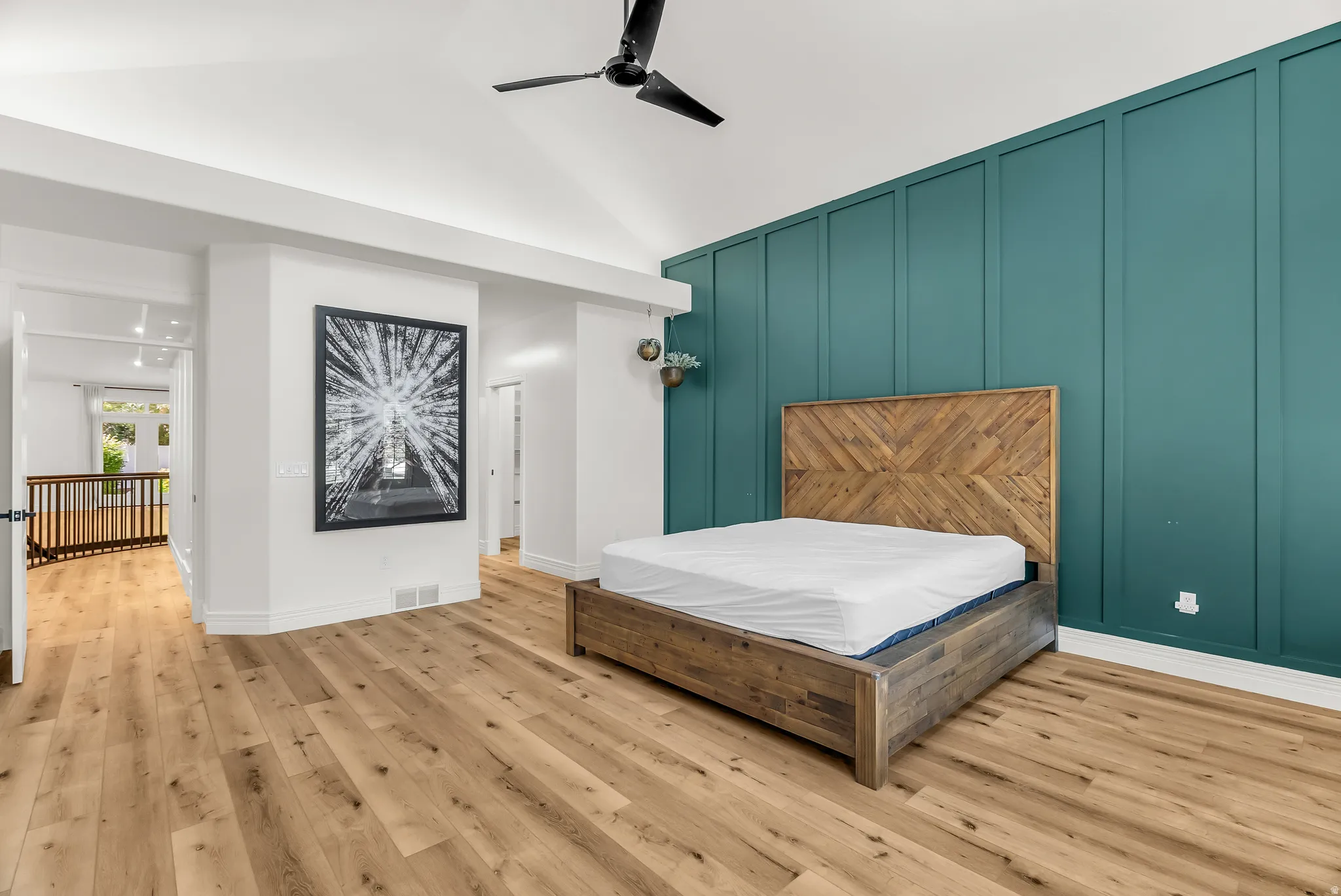 Vaulted ceiling with a ceiling fan, accent wall with vertical paneling, light wood-finish flooring, and white wall finishes