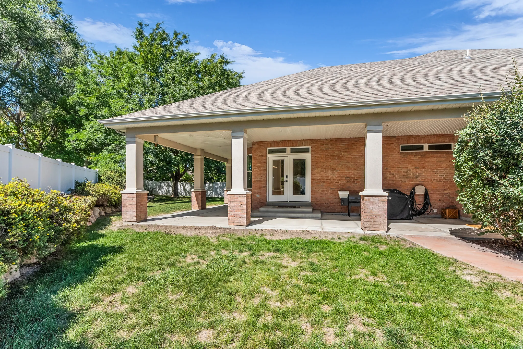 Covered patio with brick-clad columns, brick exterior, and white privacy fencing
