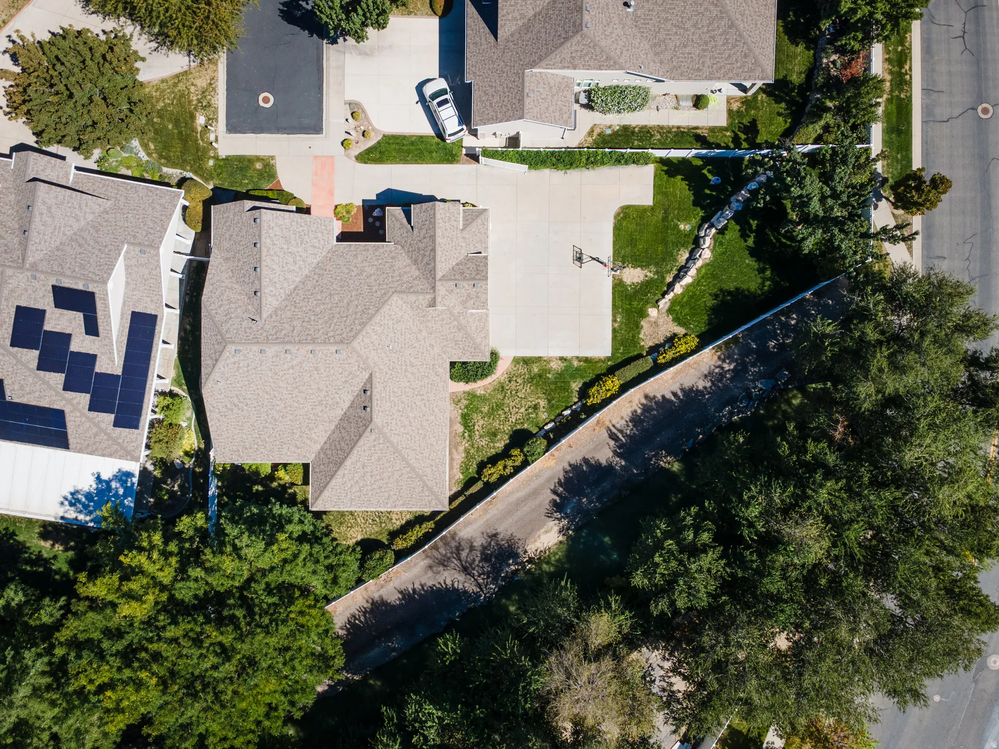 Asphalt shingle roofing, concrete driveway, manicured lawn, perimeter fencing, and mature trees