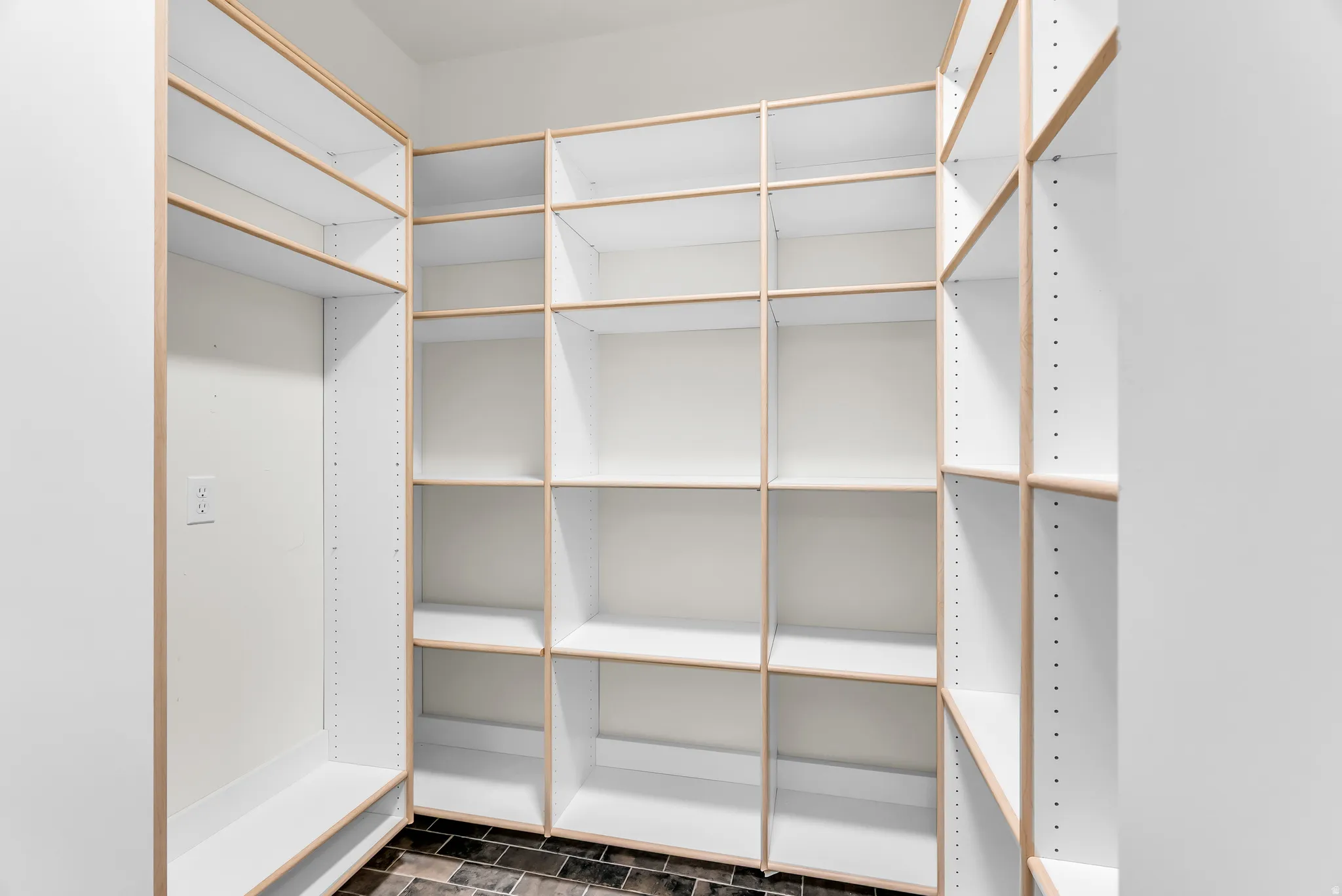 Built-in shelving units featuring a white finish with natural wood trim, dark tile flooring, and adjustable shelf heights