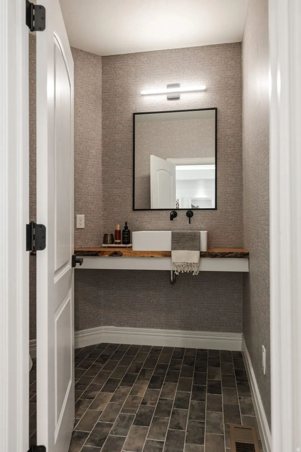 Powder room featuring a rectangular vessel sink, wood-finish countertop, wall-mounted faucet, and rectangular mirror with a black frame