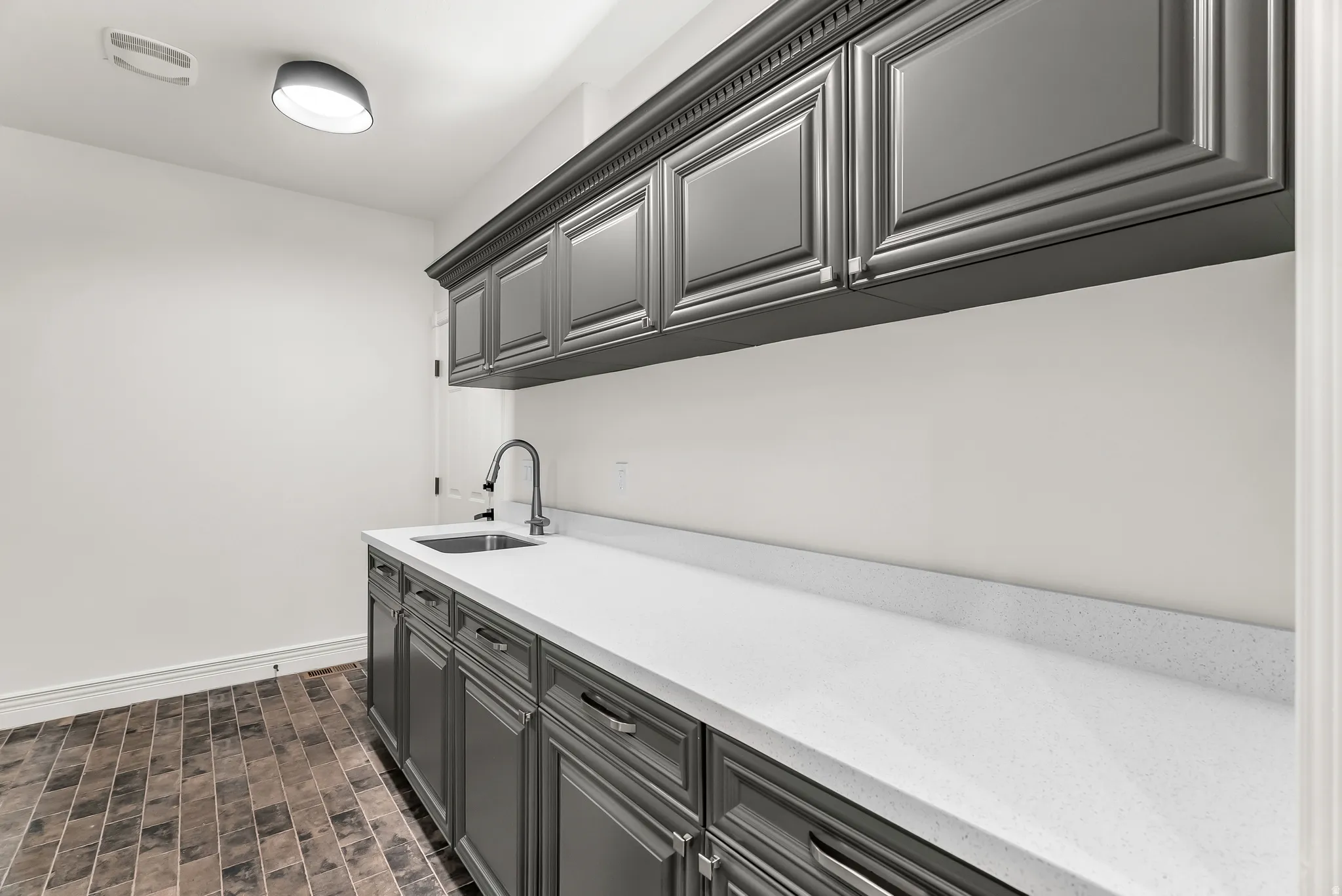 Integrated sink with a gooseneck faucet, extensive countertop space, ample cabinetry storage, and tiled flooring