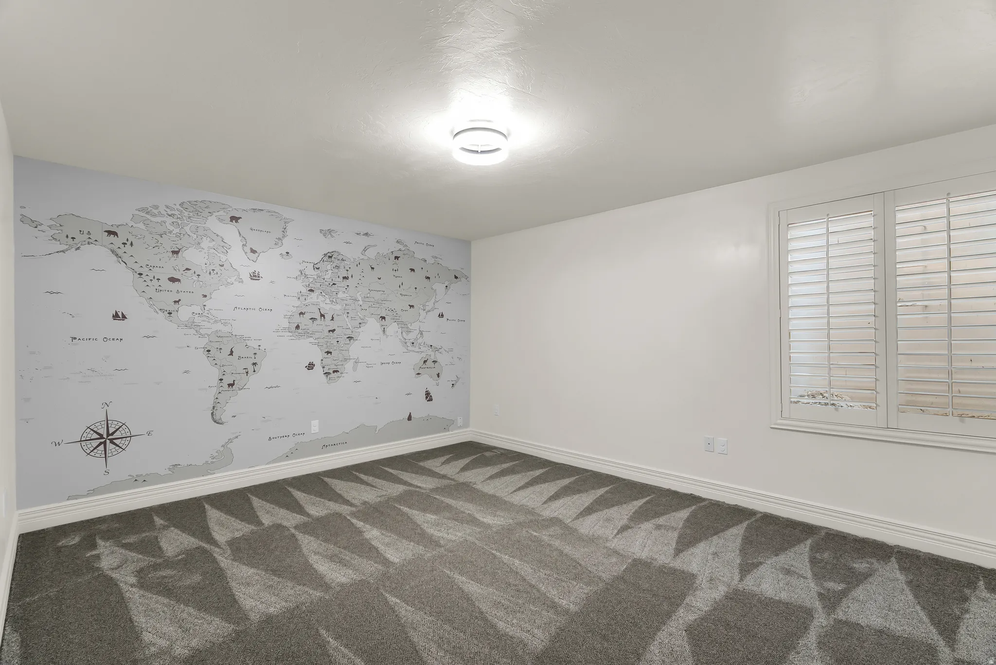 White walls with a world map accent wall, plantation shutters, and patterned gray carpet flooring