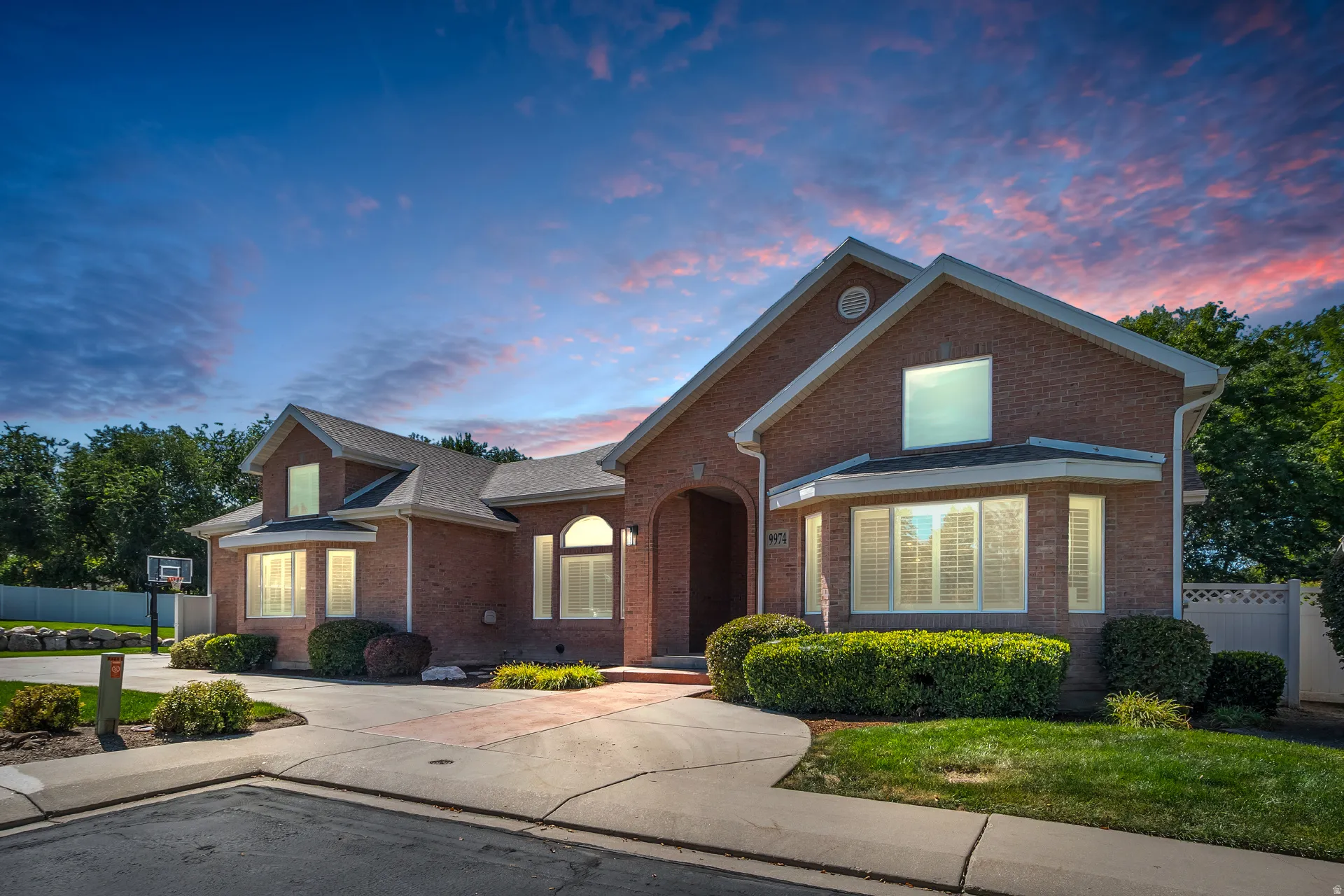 Brick exterior residence featuring a curved driveway, mature landscaping, arched entry, and a side-entry garage
