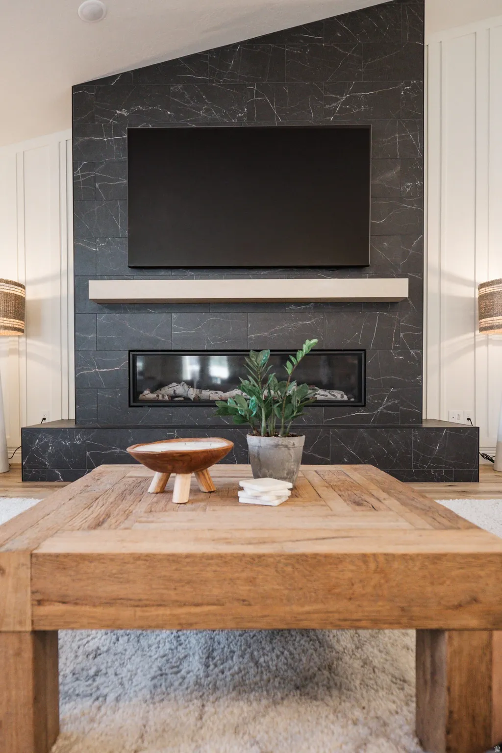 Feature wall with black marble-look tile, linear electric fireplace, integrated mantel shelf, and vertical plank accent walls