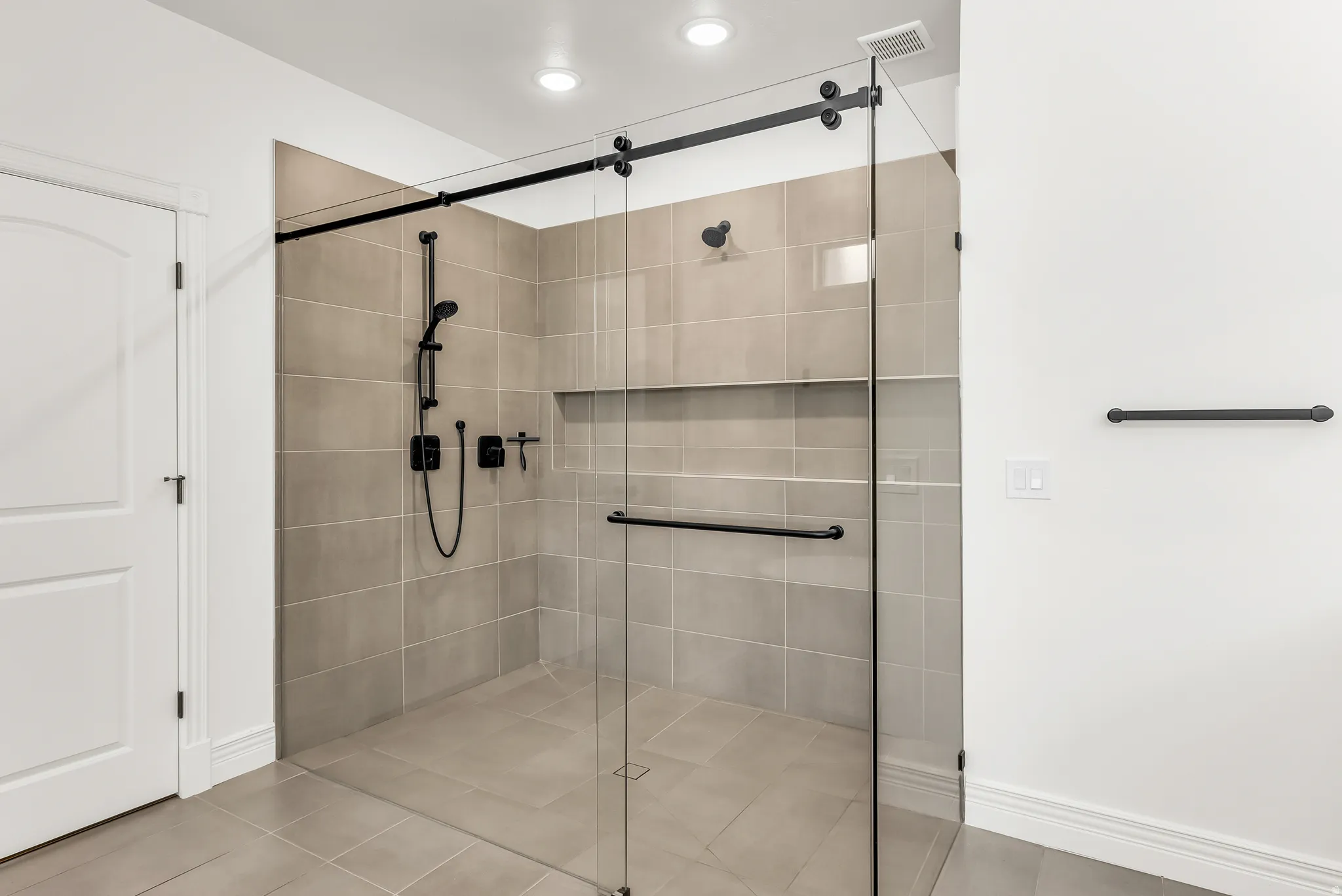 Glass-enclosed shower with matte black hardware, integrated shelf, and light-toned tile surround