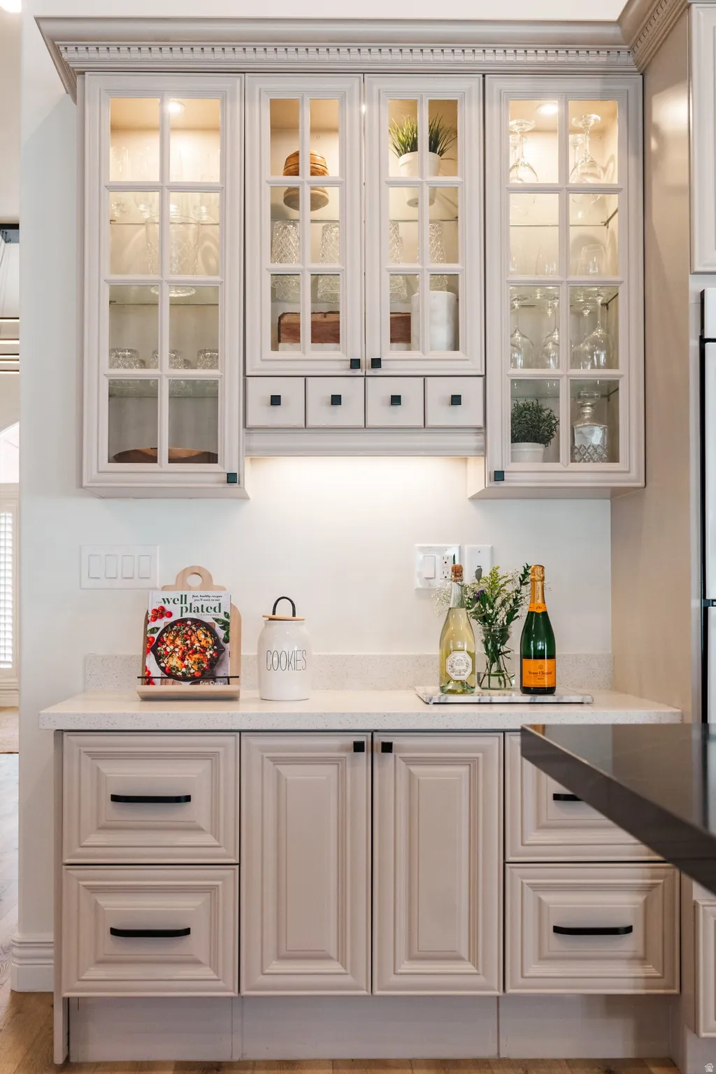 Built-in cabinetry with glass-front upper cabinets, under-cabinet lighting, and stone countertops