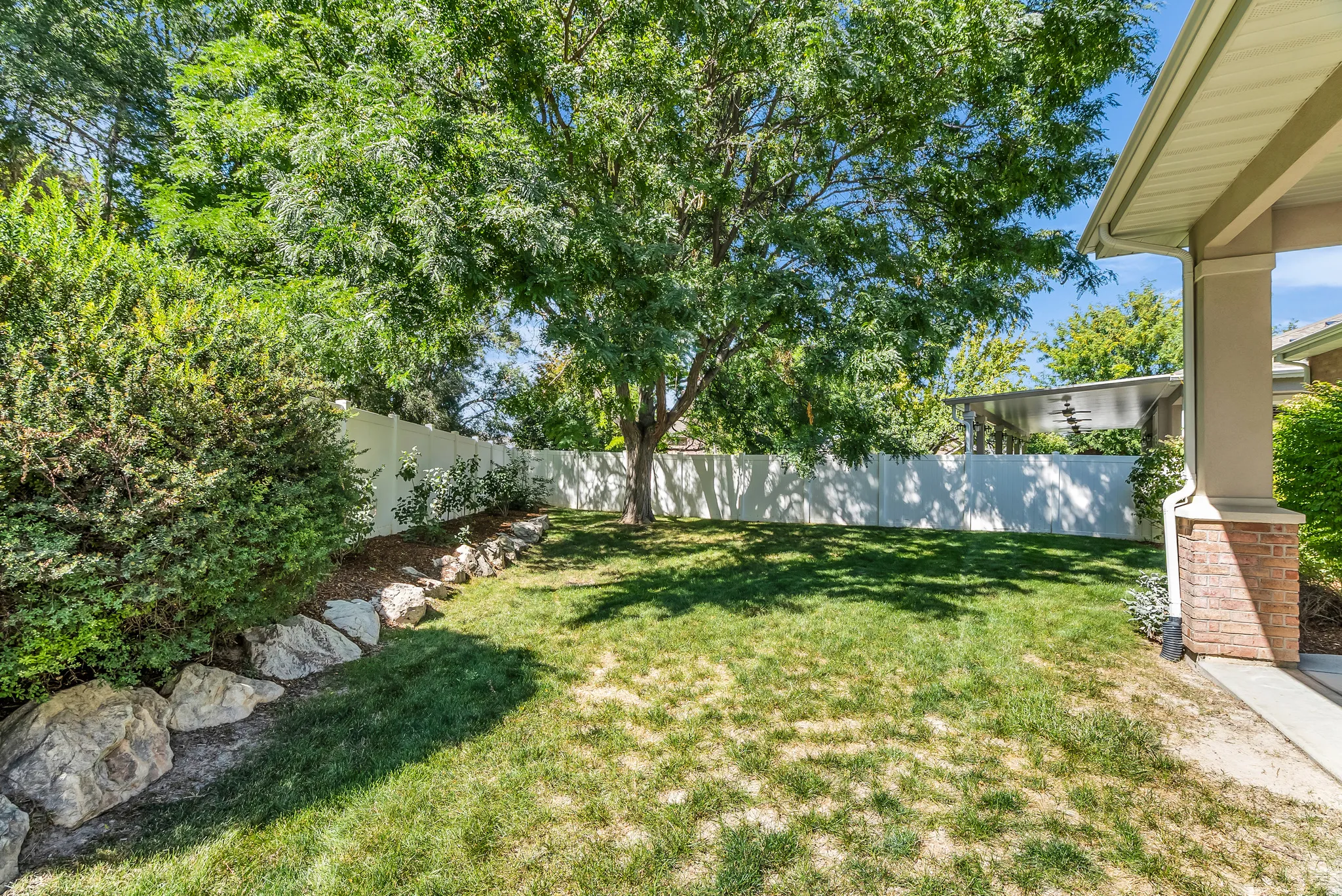 Expansive lawn area with mature trees and shrubbery, bordered by a white privacy fence