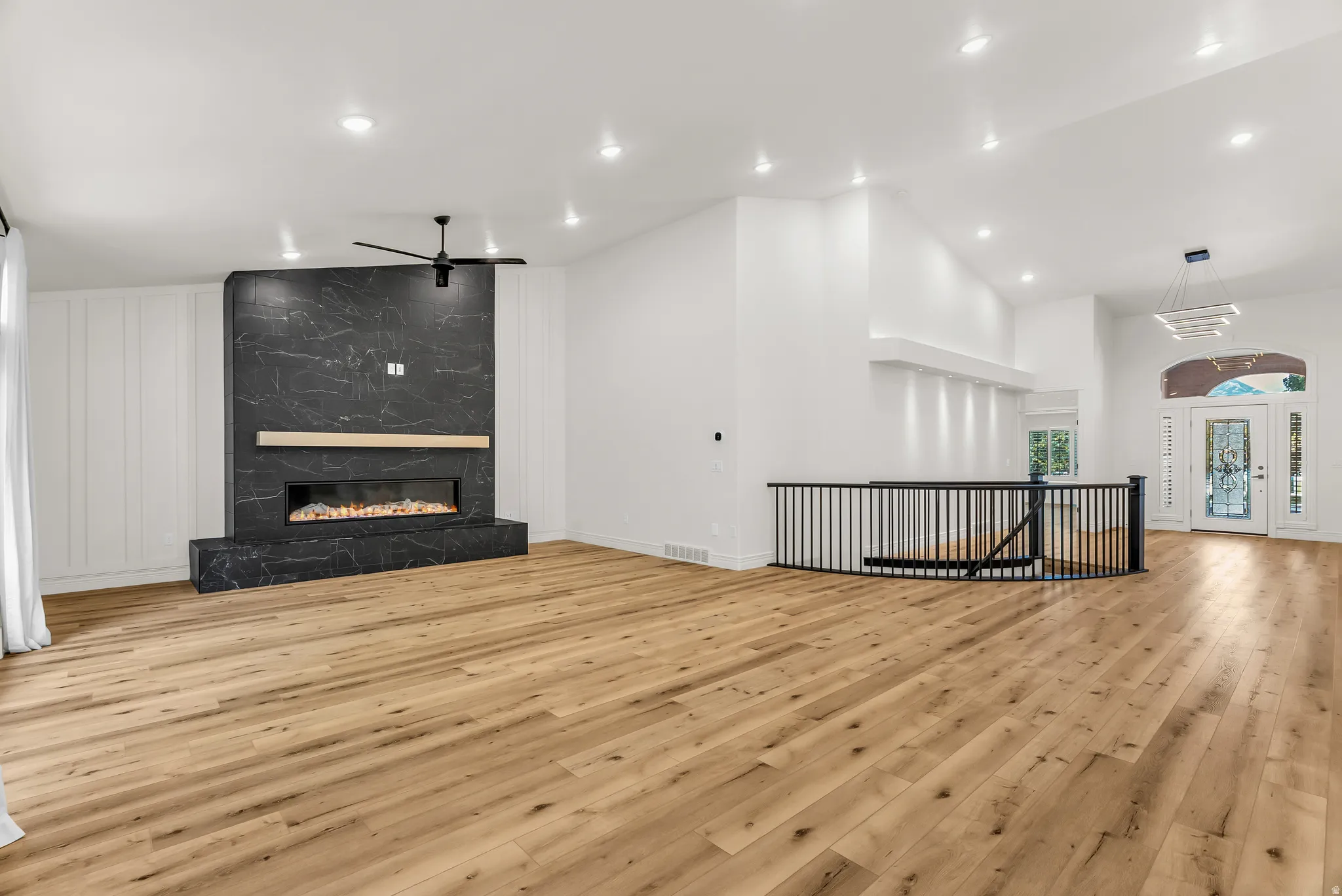 Expansive living space featuring wood-finish flooring, a contemporary fireplace with a stone surround, recessed lighting, a modern ceiling fan, and a decorative front entry door