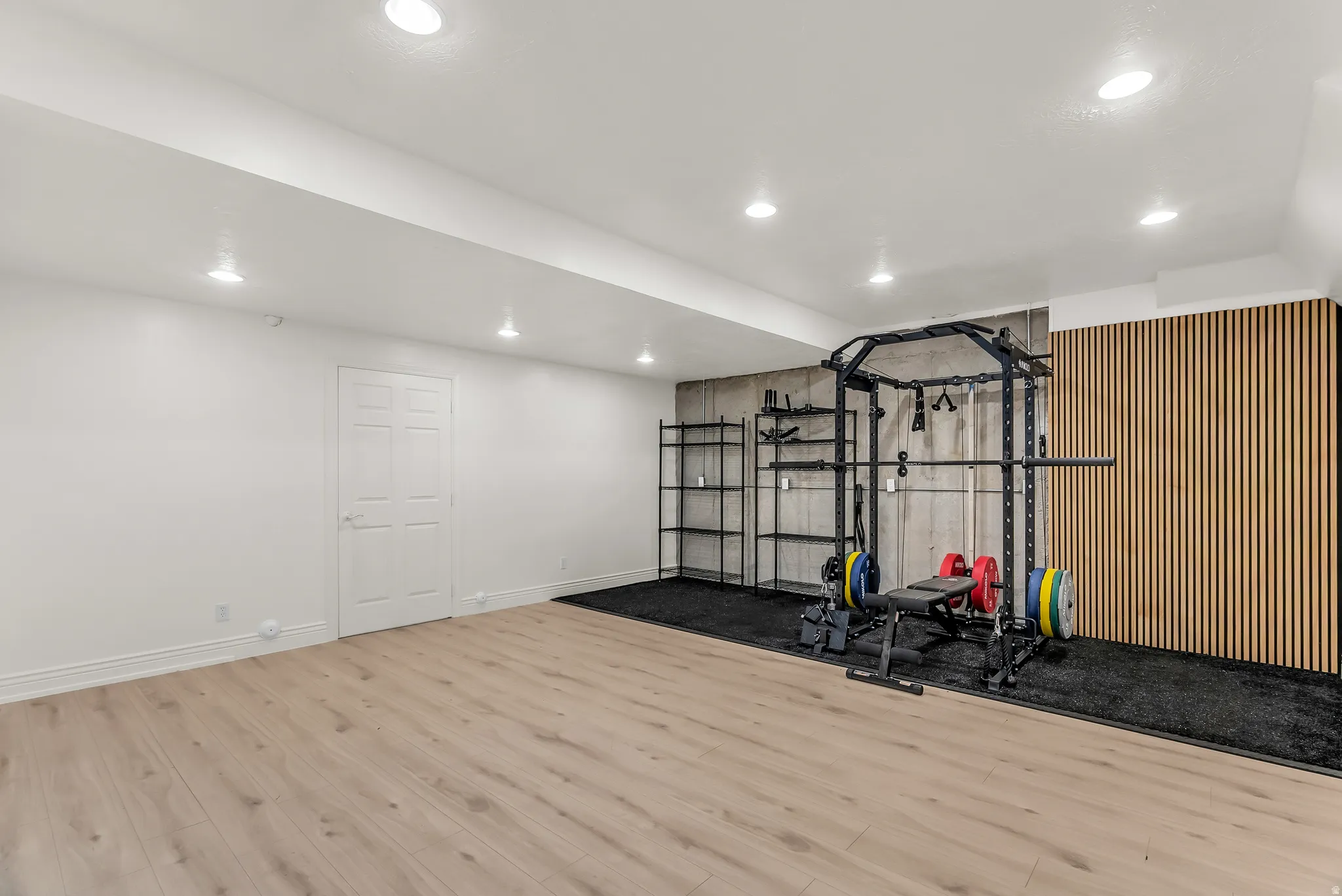 Recessed lighting, light wood-finish flooring, white paneled door, and a textured accent wall