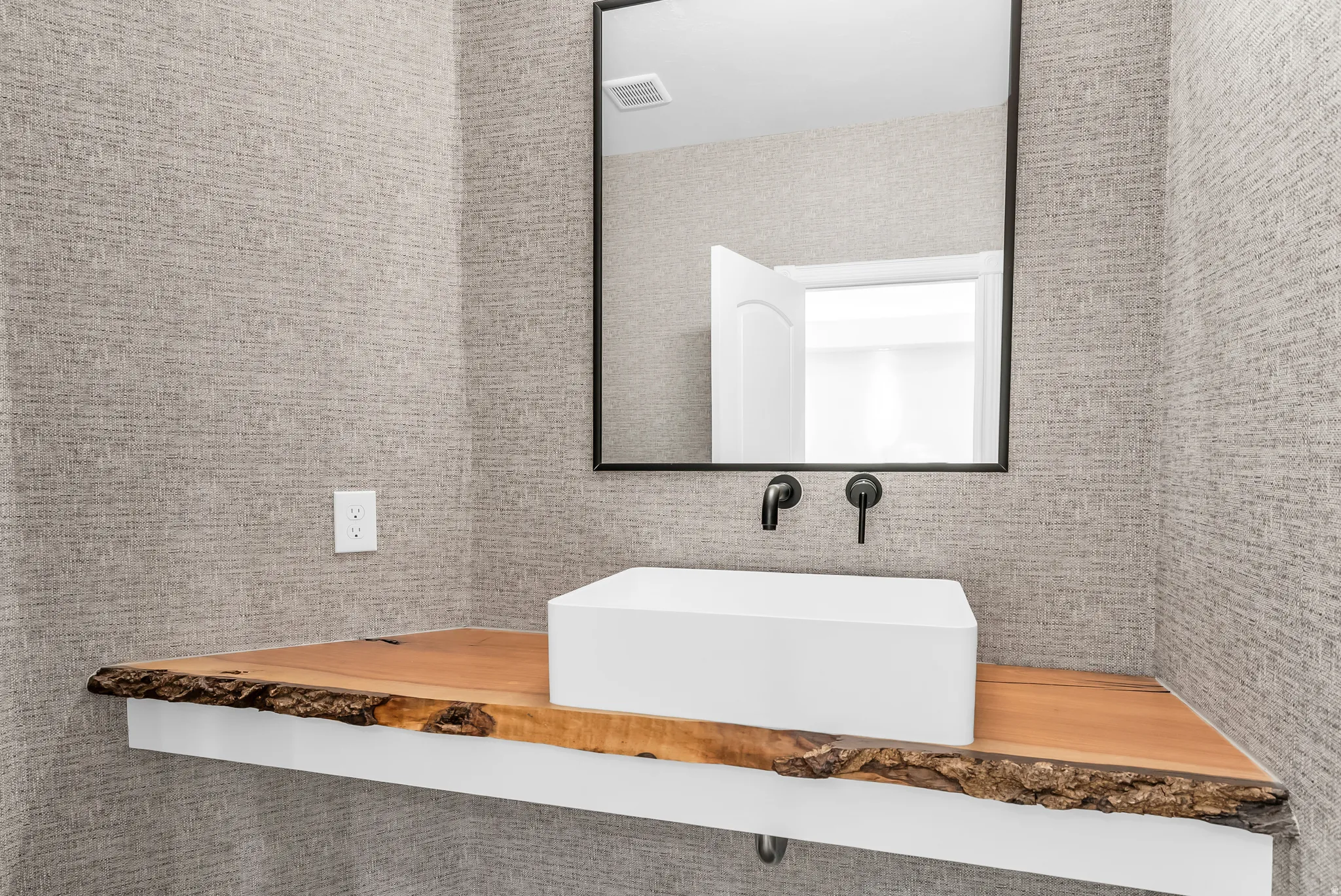 Live-edge wood vanity with a contemporary vessel sink, matte black wall-mounted faucet, and a rectangular mirror
