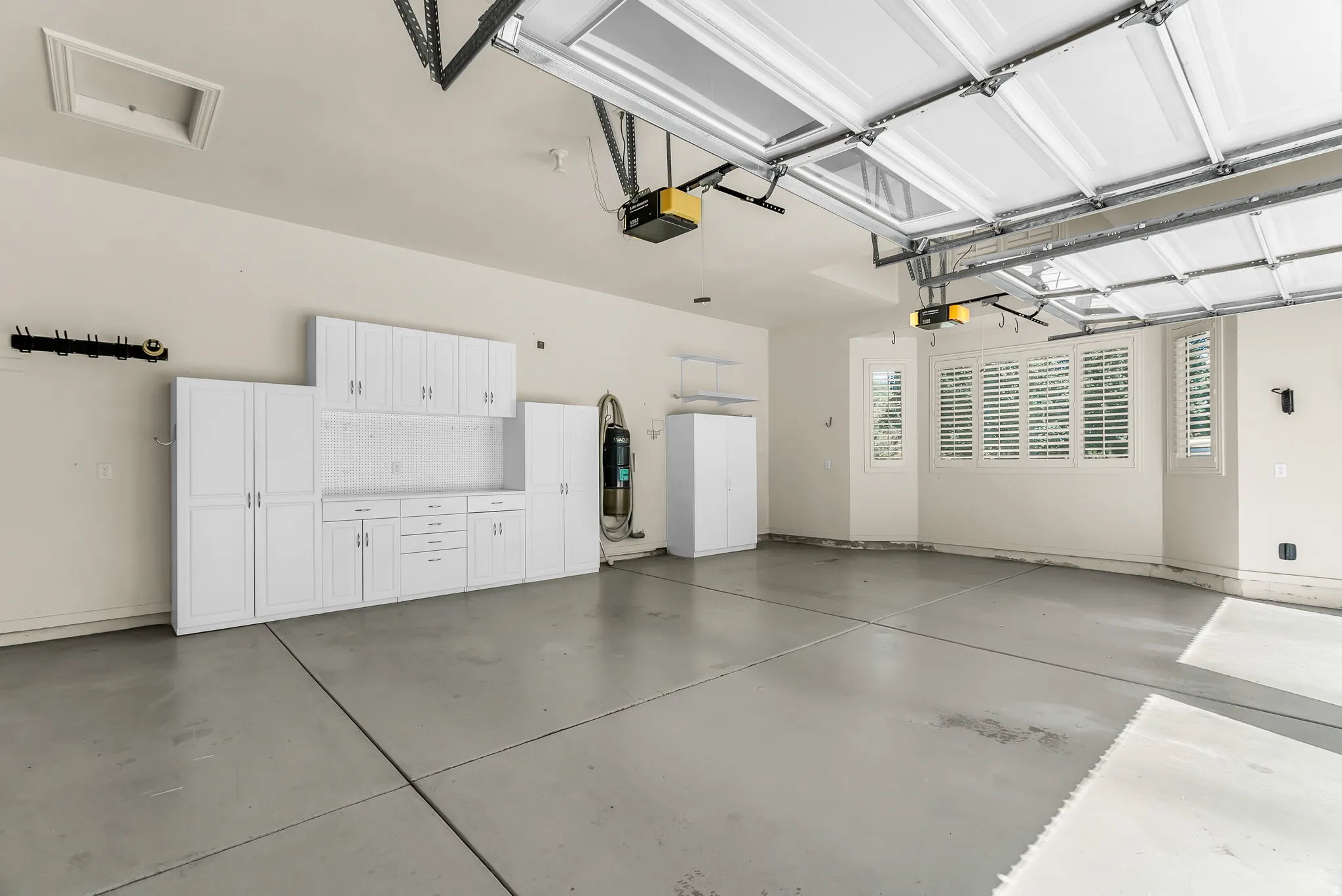 Garage featuring extensive white cabinetry, plantation shutters, and an automatic garage door opener