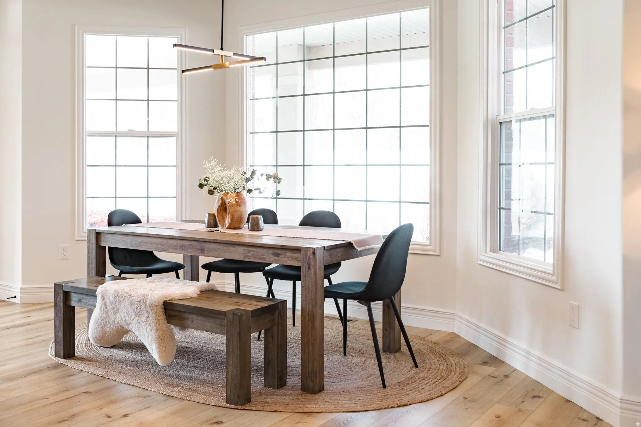 Expansive bay window featuring grid-patterned panes, light wood-finish flooring, and a contemporary linear pendant light fixture
