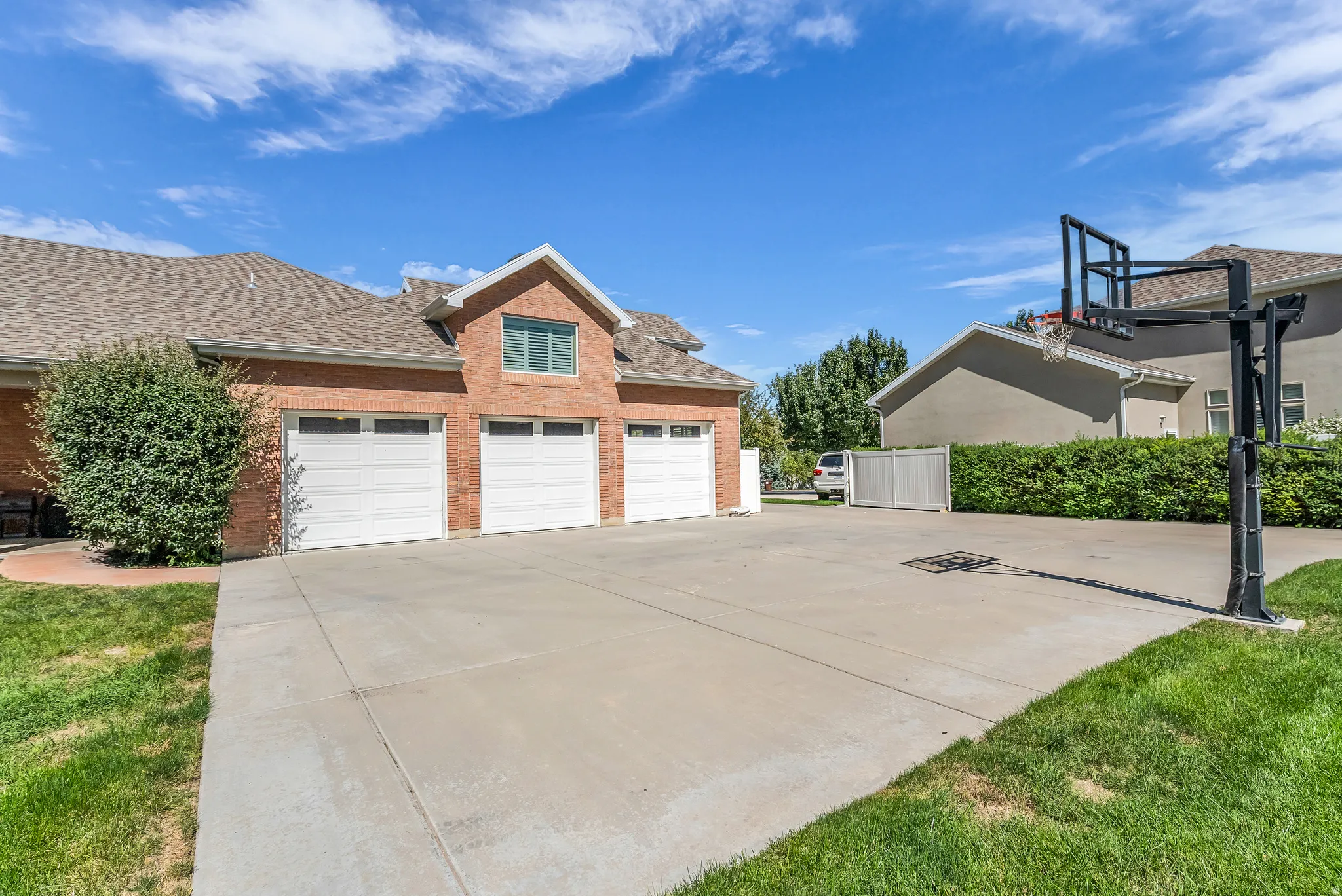 Brick exterior with multiple garage bays, expansive concrete driveway, basketball hoop, and manicured landscaping