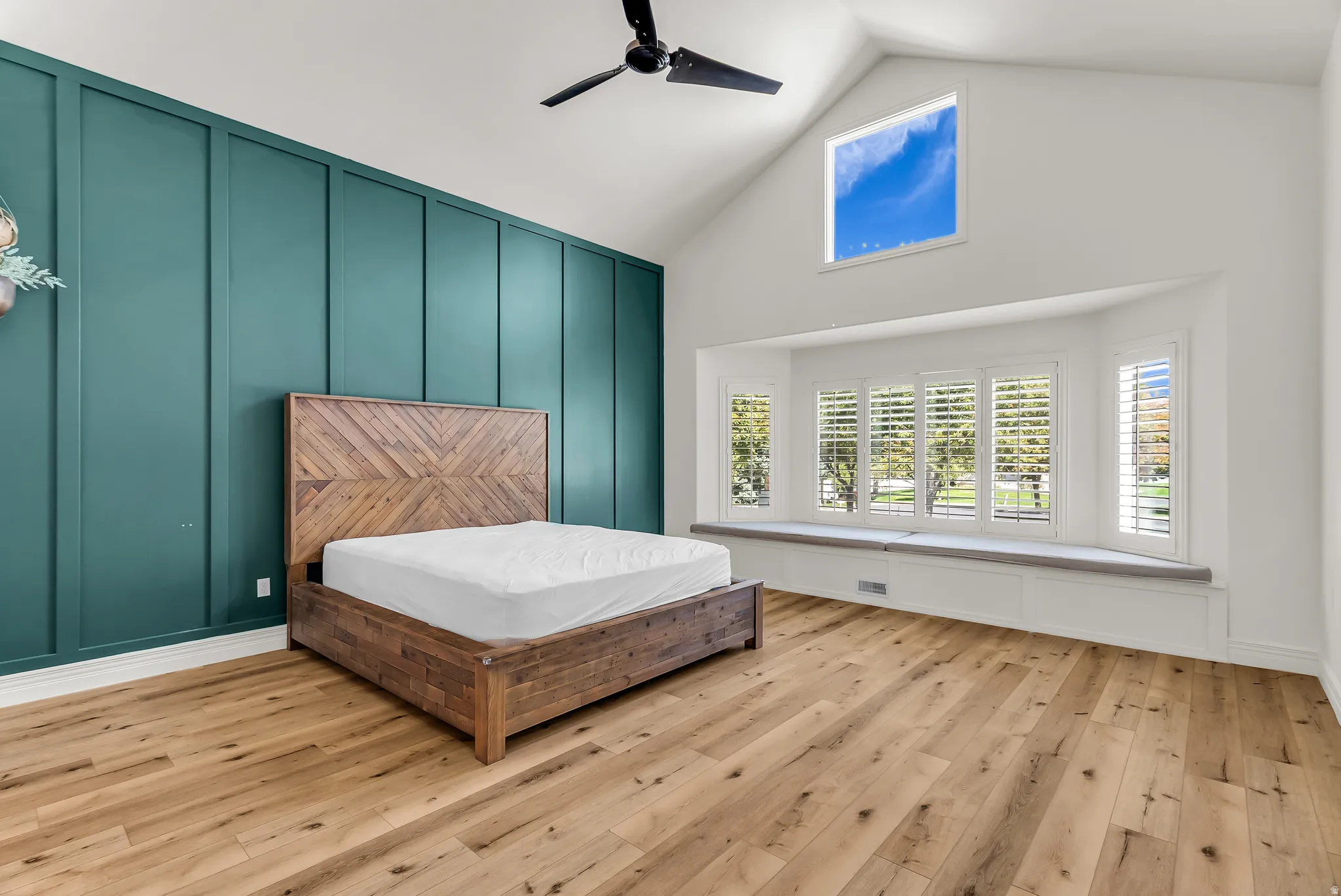 Vaulted ceiling with an upper transom window, wood-finish flooring, accent wall with vertical paneling, and a built-in window seat with storage