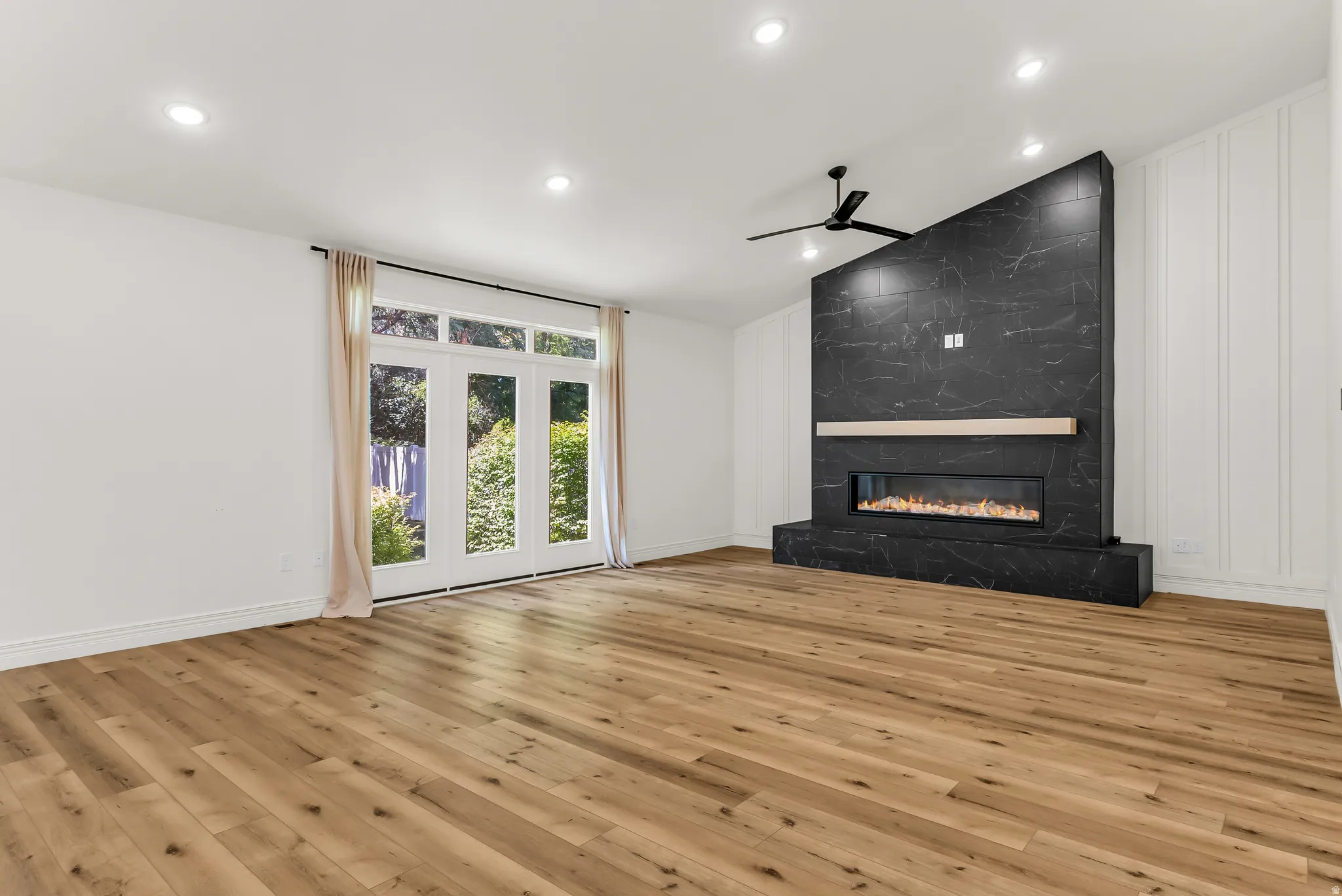 Spacious room featuring wood-finish flooring, a contemporary black marble-look fireplace, a wood mantel, and large glass panel doors