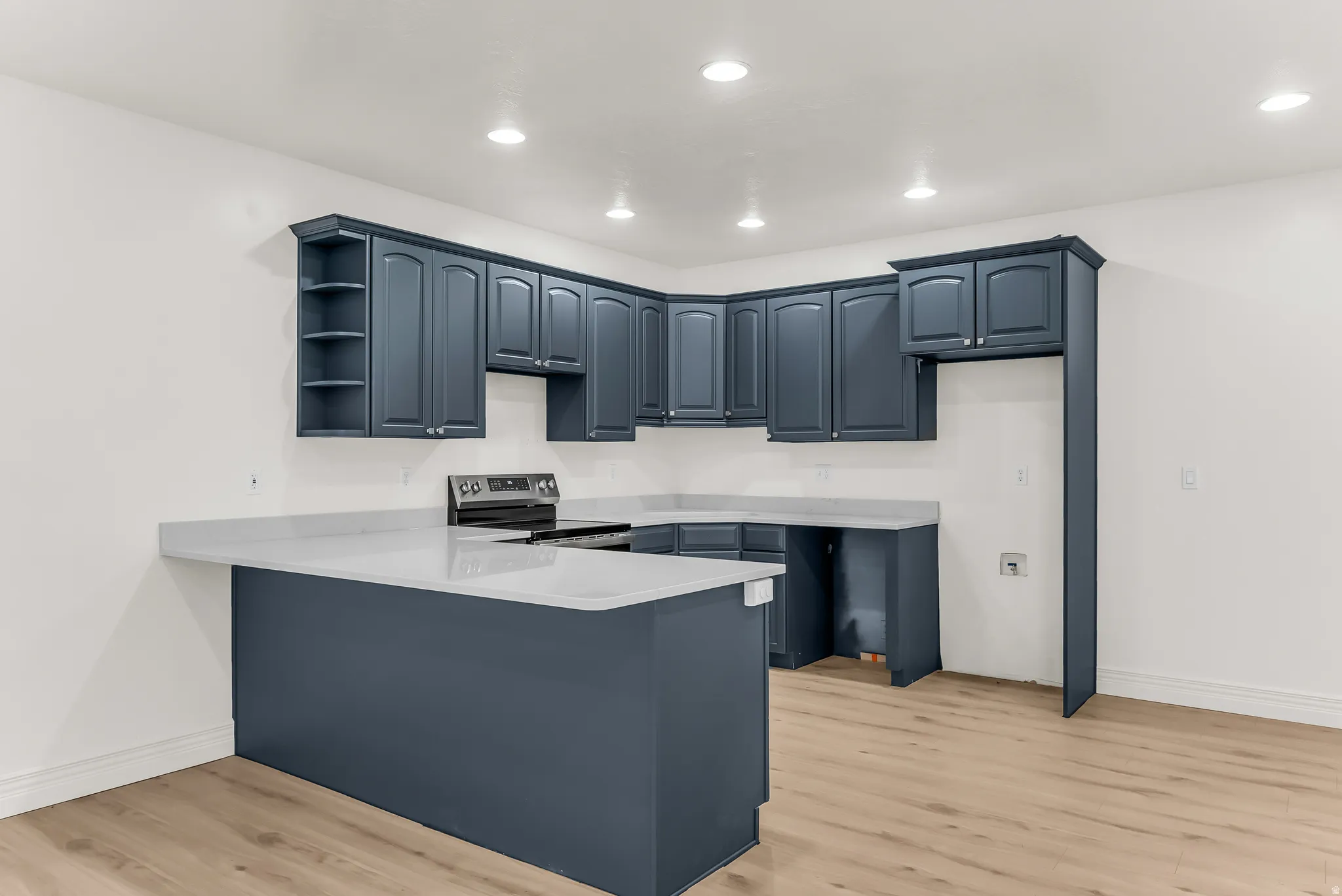 Kitchen featuring blue cabinetry, light-toned countertops, a built-in range, wood-finish flooring, and recessed lighting