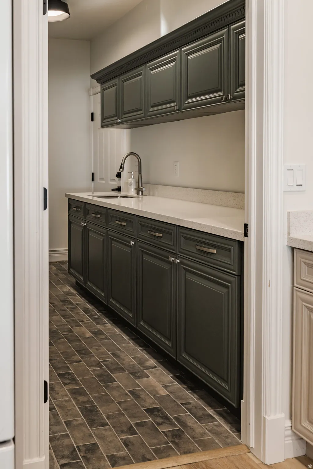 Cabinetry with crown molding, integrated sink, brushed nickel faucet, light-toned countertop, and tile flooring